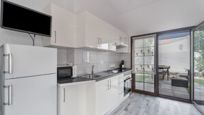 A modern kitchen with white cabinets, a flat-screen TV, a microwave, and a sink.