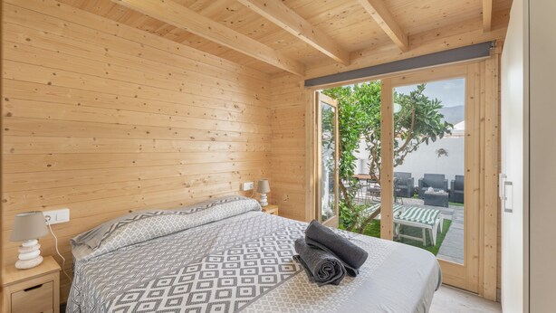 A wooden-paneled bedroom with a bed, bedside lamps, and a view of an outdoor patio with furniture.