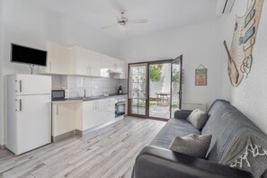 A modern kitchen with white cabinets, a flat-screen TV, and a ceiling fan.