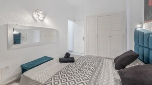 A bedroom with a bed, a bench, a mirror, a wardrobe, and a door.