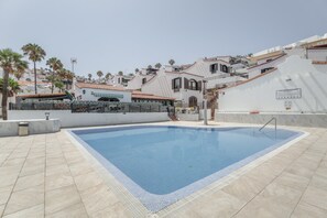 A swimming pool with a tiled deck, surrounded by buildings with balconies and palm trees.