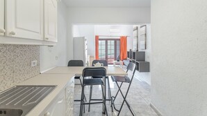 Una cucina moderna con zona pranzo, pensili bianchi, un lavello e una finestra con tende arancioni.