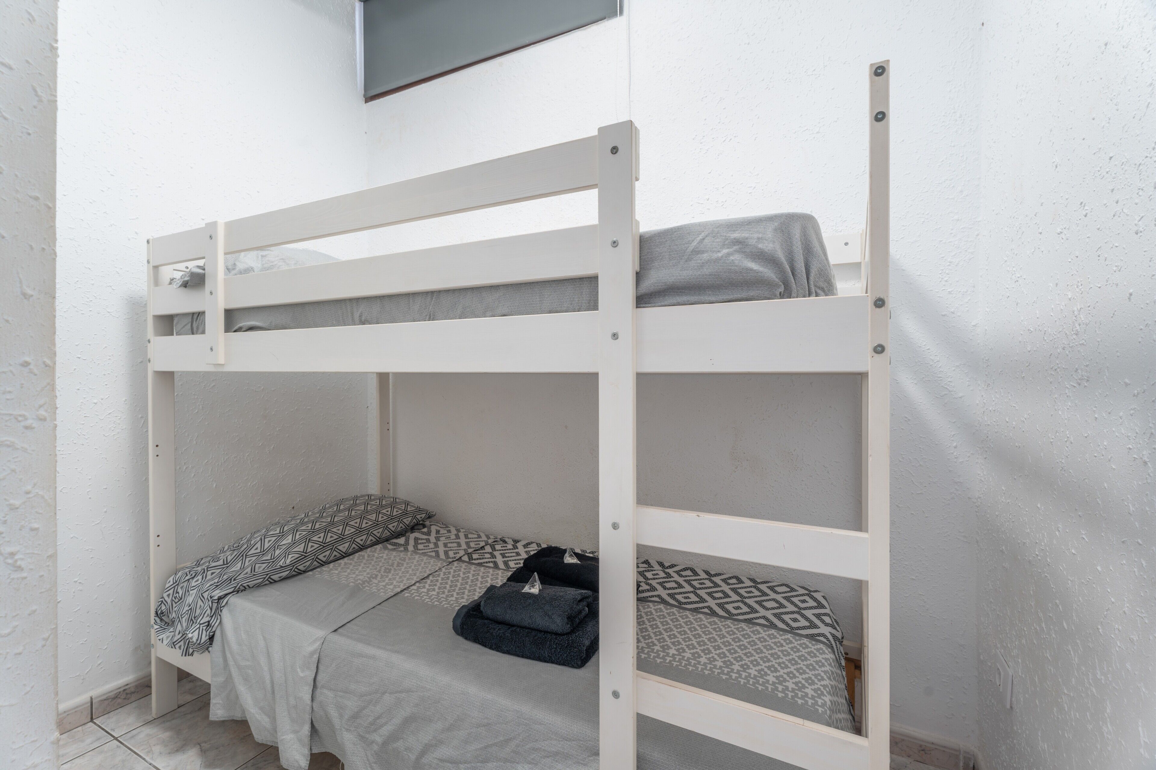A bunk bed with a grey mattress and patterned bedding.