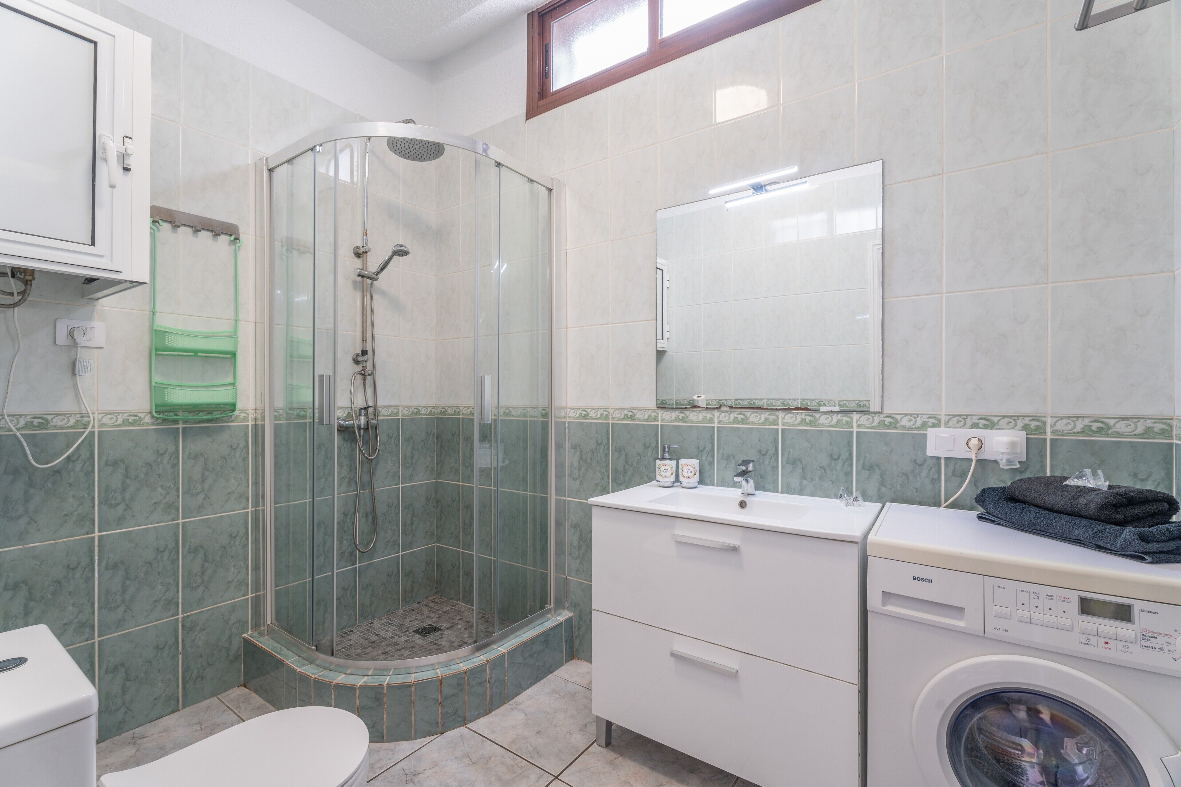 A bathroom with a glass-enclosed shower, a washing machine, and a toilet.
