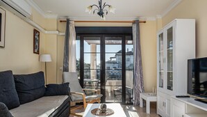 A living room with a sofa, armchairs, a coffee table, a TV, and a balcony with a view.