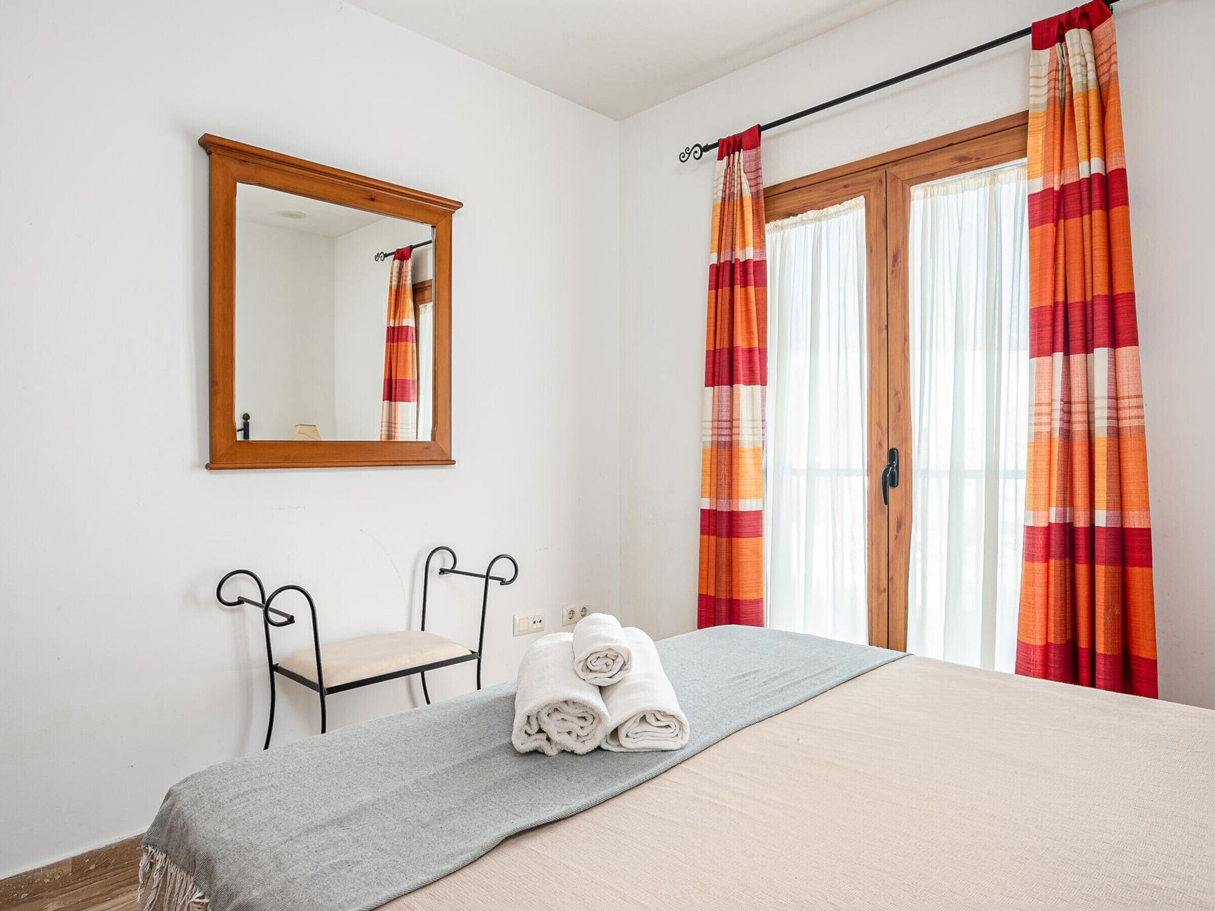 Un dormitorio con una cama, un espejo, una silla y una ventana con cortinas.
