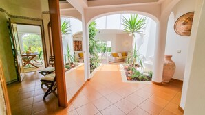 Um interior com sala de jantar, sala de estar e corredor com arcos e plantas.