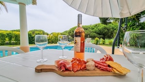 Uma mesa com uma garrafa de vinho, duas taças e uma tábua de madeira com diversos queijos e carnes.