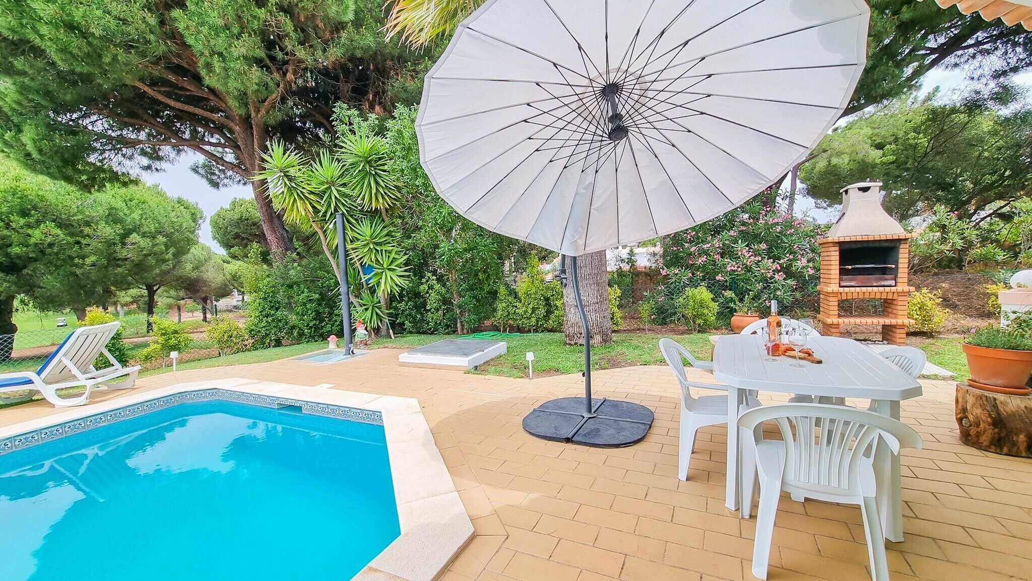 Un espace piscine aménagé avec une table et des chaises, un grand parasol et un four en briques.
