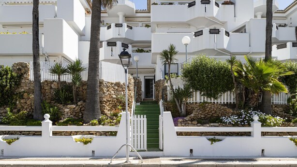 Un edificio blanco con varios balcones, un muro de piedra y una entrada verde.