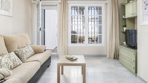Una sala de estar con sofá, una mesa con un plato decorativo, televisor sobre un mueble bajo y un ventanal con cortinas.