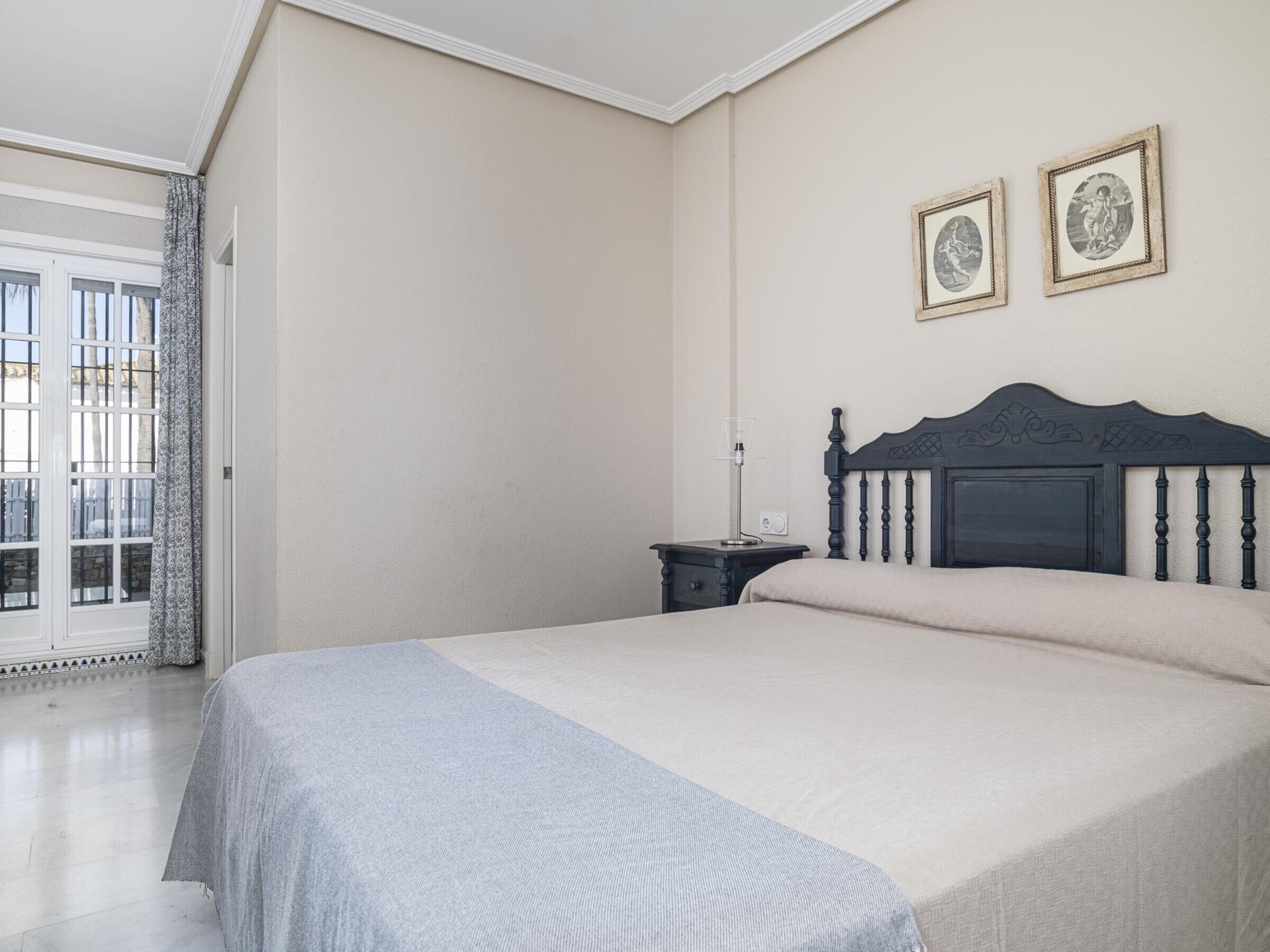 Un dormitorio con una cama, una mesita de noche, una lámpara y dos cuadros en la pared.