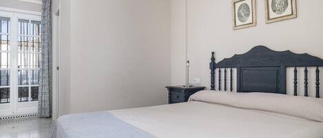 Un dormitorio con una cama, una mesita de noche, una lámpara y dos cuadros en la pared.
