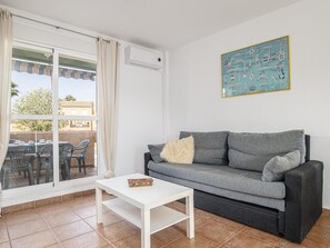 A living room with a grey sofa, a white coffee table, and a large window with curtains.