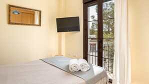 Een slaapkamer met een bed, een televisie, een balkon met uitzicht en een raam met gordijnen.