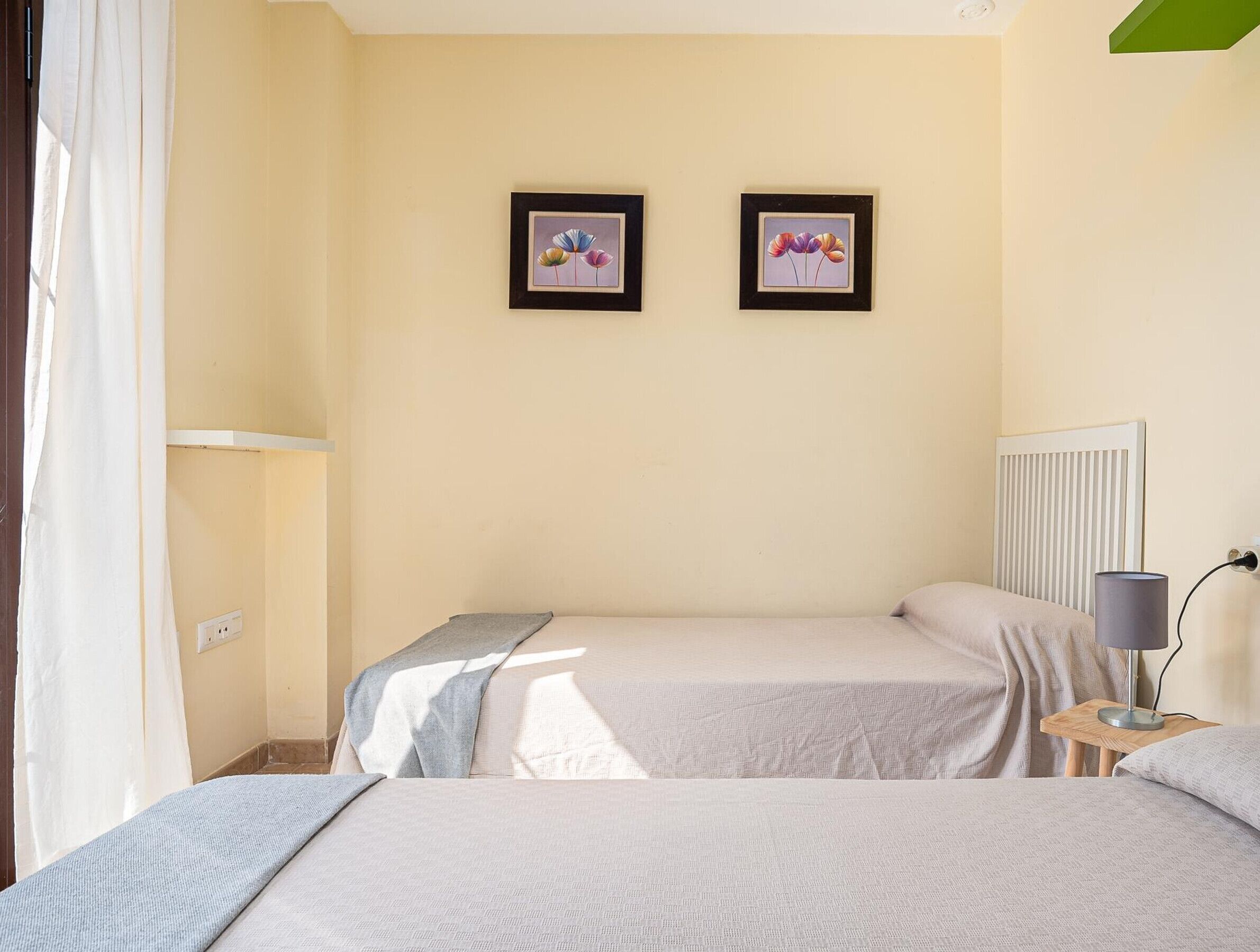 A bedroom with two beds, a radiator, a lamp on a bedside table, and two framed pictures on the wall.