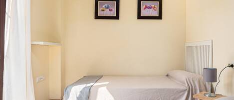 A bedroom with two beds, a radiator, a lamp on a bedside table, and two framed pictures on the wall.