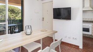 A dining area with a wooden table and chairs, a TV mounted on the wall, and an air conditioning unit above the door.