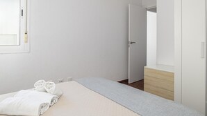 A bedroom with a bed, a bedside table, a wardrobe, a window, and a door.