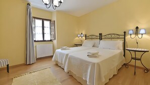 A double bed with white linens, two bedside tables with lamps, a radiator, a window with curtains, and a small striped chair. - Apartment 'Puente Del Narcea 3' with Mountain Views, Private Terrace and Wi-Fi (Cibuyo)
