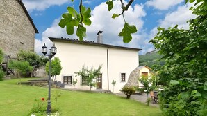 A traditional building with a white facade, a stone wall, and a small garden area with a lamp post. - Apartment 'Puente Del Narcea 3' with Mountain Views, Private Terrace and Wi-Fi (Cibuyo)
