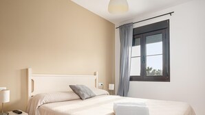 A bedroom with a bed, a nightstand, a lamp, a window with curtains, and a view of the outside.