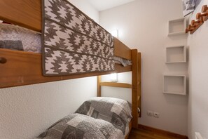 Una cama individual con ropa de cama estampada, cabecera de madera y una pequeña estantería en la pared.