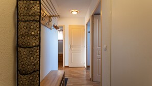 Um corredor com parede estampada, um banco de madeira, uma porta no final e uma luminária no teto.