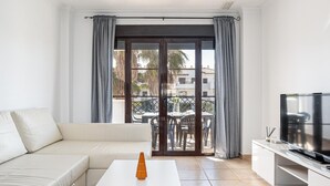 En moderne stue med en hvid sofa, et sofabord, et fjernsyn og en balkon med et bord og stole.