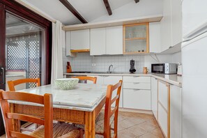 Een keuken met witte kastjes, een eettafel met stoelen, een magnetron en een waterkoker.