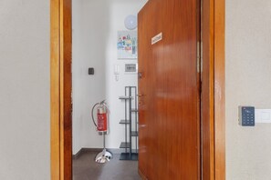 Un pasillo con una puerta de madera, un extintor, un teléfono y un interfono instalado en la pared.