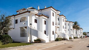Une rangée de bâtiments blancs dotés de balcons, un ciel dégagé et une rue devant.