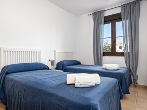 A hotel room with two beds, white radiators, a window with curtains, and a view of buildings outside.