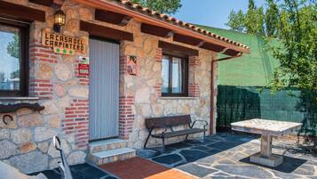A stone building with a sign reading 'La Casa del Carpintero,' a bench, a table, and a pair of scissors on the ground.
