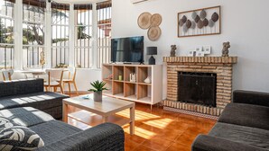 A modern living room with a fireplace, a television, and a dining area with a table and chairs. - Luxury villa in Chiclana, close to the beach (Chiclana de la Frontera)