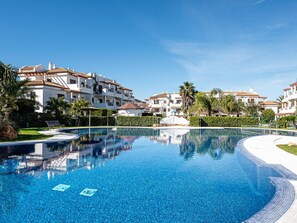 A swimming pool with clear blue water, surrounded by white buildings with red-tiled roofs and balconies.