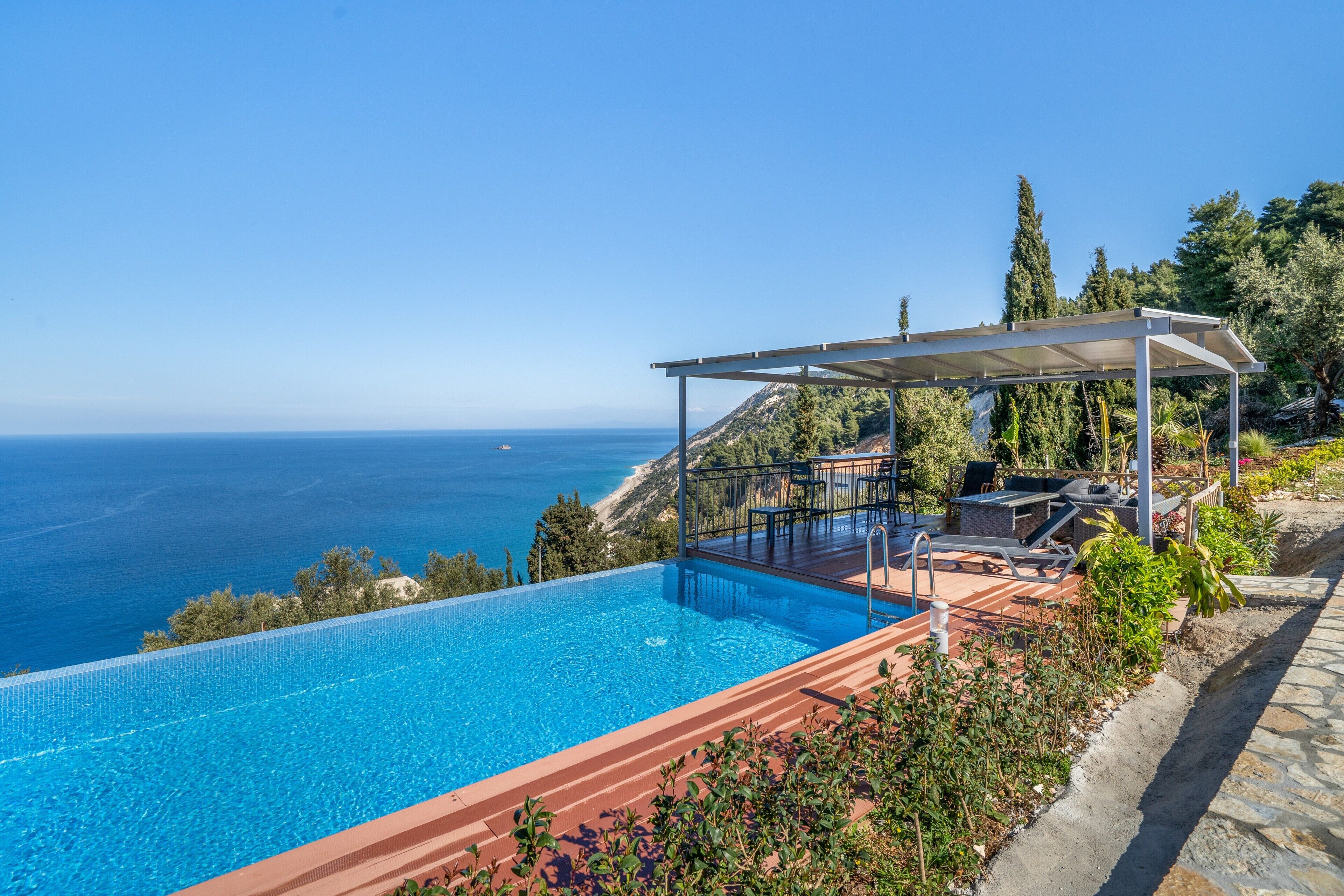 Una piscina con vistas al mar, un área de descanso cubierta con sillones de relax y un sendero de piedra.