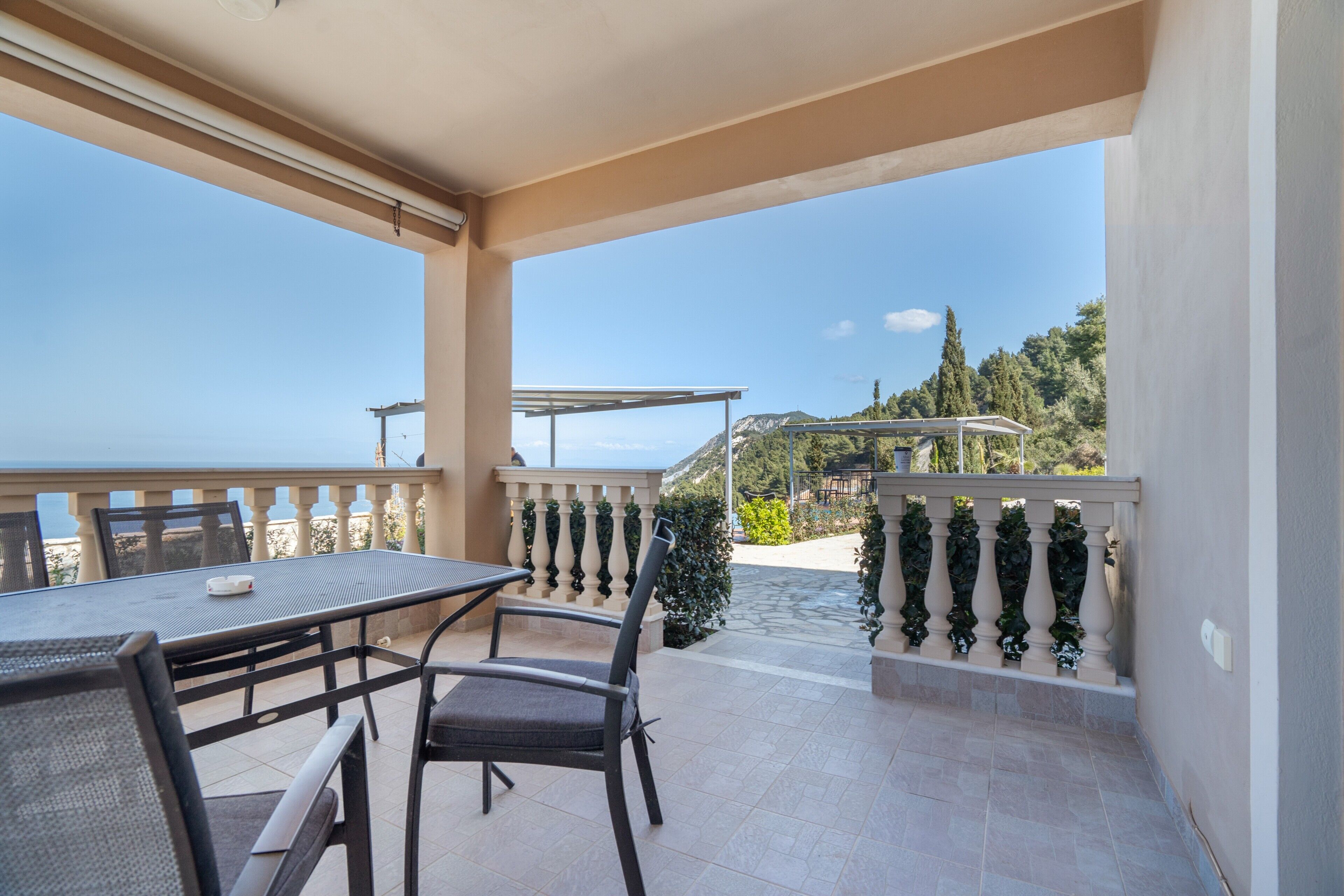 Un balcone con tavolo e sedie, vista mare e una pergola.