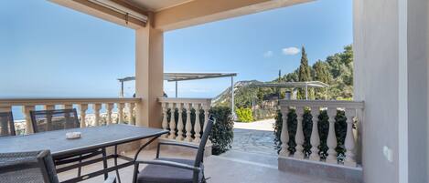 Un balcone con tavolo e sedie, vista mare e una pergola.
