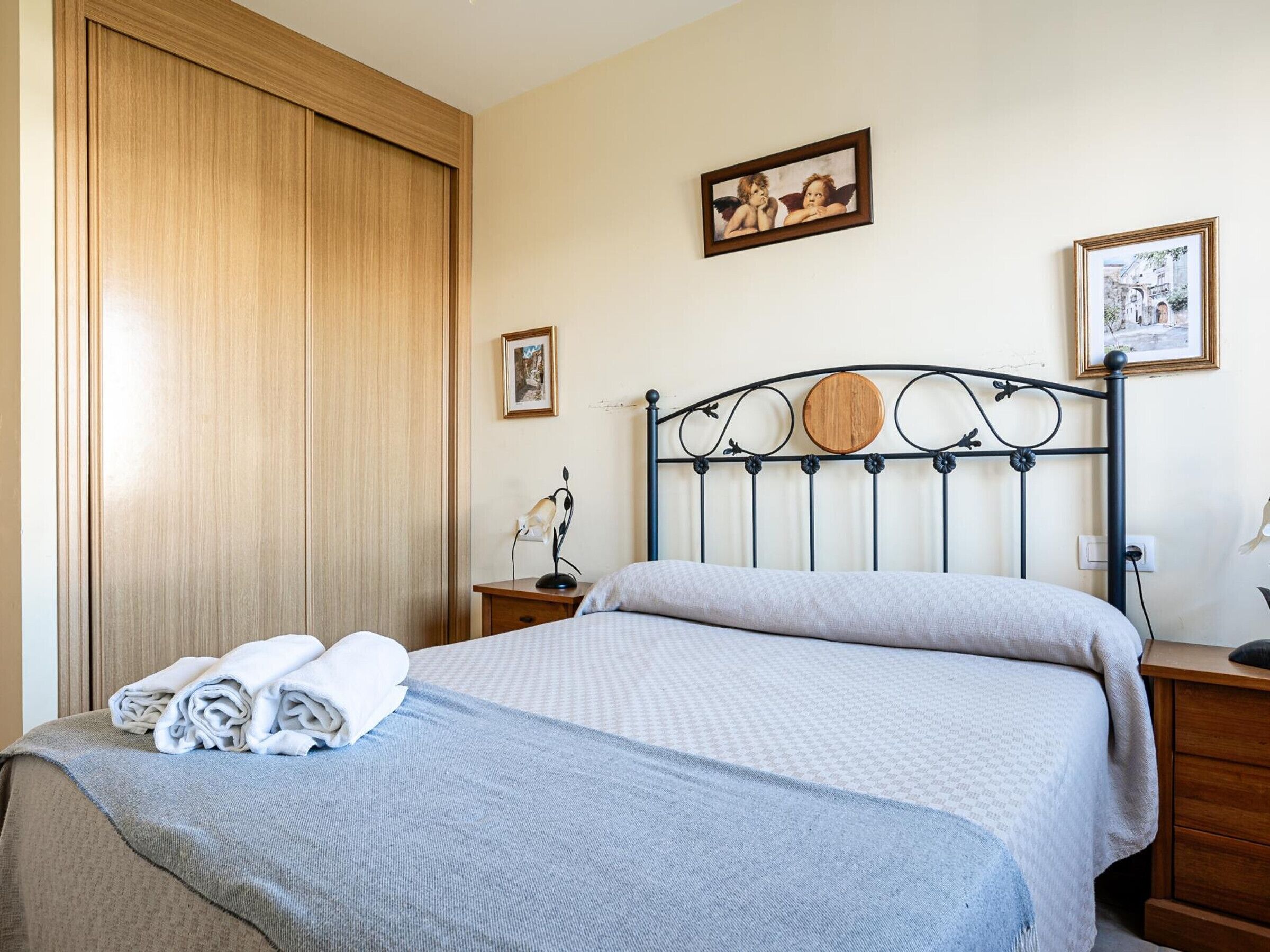 A neatly made bed with a grey and white checkered bedspread, a wooden headboard with circular decorations, a nightstand with a lamp, and two framed pictures on the wall.