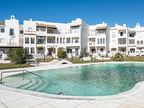 A pool area with a clear blue pool, surrounded by white buildings with balconies and a central column.