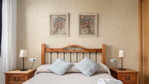 A neatly made bed with two pillows, a wooden headboard, and two bedside tables with lamps. There are two framed floral paintings on the wall above the bed.