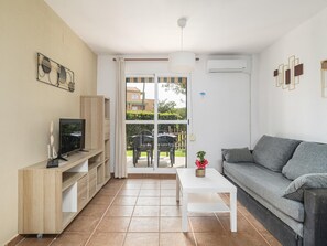 Un salon moderne avec un canapé, un téléviseur et un coin repas visible à travers une porte vitrée.