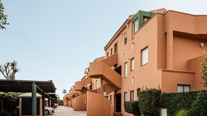 A row of modern buildings with balconies, a covered parking area, and greenery.