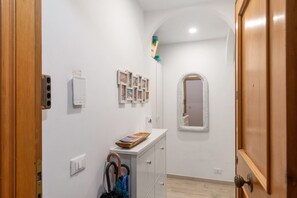 Un couloir avec une porte en bois, un mur blanc orné d’un tableau encadré, une armoire blanche et un miroir.
