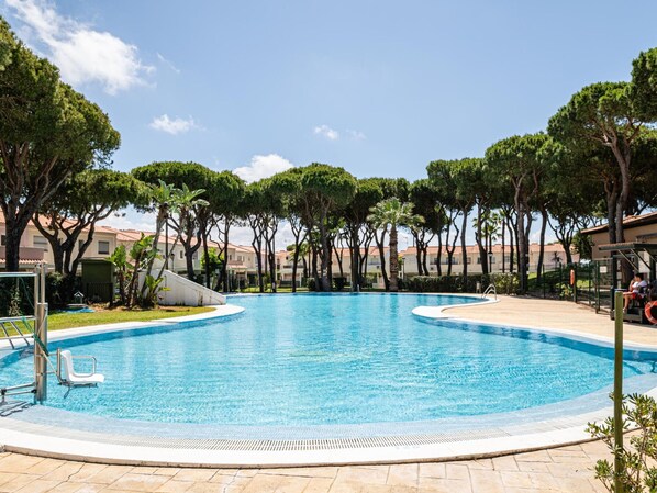 Une piscine entourée d’une terrasse, d’arbres et d’un bâtiment en arrière-plan.