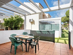 Une terrasse avec une table ronde et des chaises, un mur blanc et une clôture verte.
