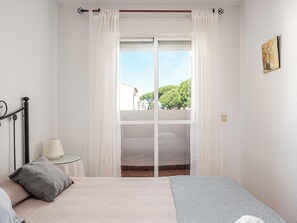 Une chambre à coucher avec un lit, une table de chevet avec une lampe, une fenêtre avec des rideaux et un tableau au mur.