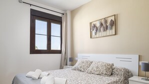 Un dormitorio con cama, mesita de noche, ventana con cortinas y un adorno en la pared.