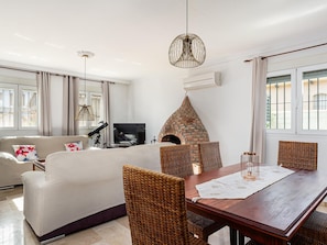 A living room with a sofa, a dining table with chairs, a TV, and a brick oven.